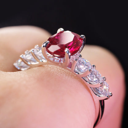 Oval red zircon ring with simulated diamond accents on a finger 