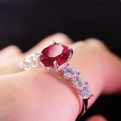 Oval red zircon ring with simulated diamond accents on a finger 