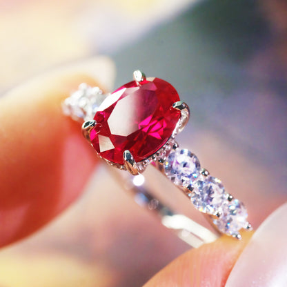 Oval red zircon ring with simulated diamond accents held between fingers.