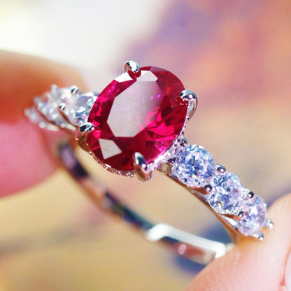 Oval red zircon ring with simulated diamond accents held by a hand.