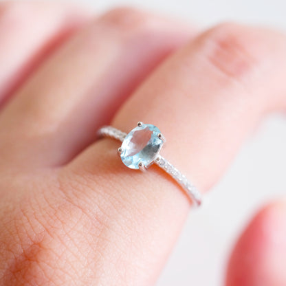 Oval aquamarine silver ring with simulated diamond accents on a finger 