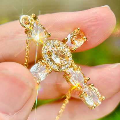 Gold crystal cross necklace with  champagne gemstones held in a hand 