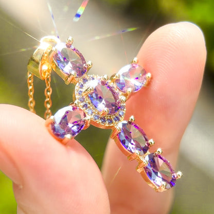 Gold cross pendant necklace with purple gemstones held between fingers 